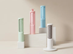 Four compact cylindrical personal care devices in pastel shades of mint green, pink, light blue, and white, arranged on white display blocks against a warm beige background.