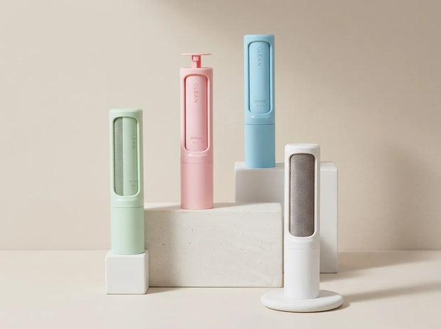 Four compact cylindrical personal care devices in pastel shades of mint green, pink, light blue, and white, arranged on white display blocks against a warm beige background.