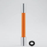 An orange cylindrical cosmetic tube with shiny silver metallic caps, shown standing upright on a light gray background with a small black ring accessory placed beside it.