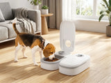 A small brown, white, and tan dog is eating from a white automatic pet feeder in a bright, modern living room with light wood floors and a gray sofa.