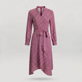 A long-sleeve wrap dress with a geometric pattern in pink and dark red, featuring a tie belt at the waist and a split neckline, shown against a light gray background.