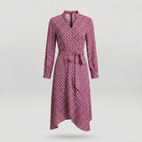 A long-sleeve wrap dress with a geometric pattern in pink and dark red, featuring a tie belt at the waist and a split neckline, shown against a light gray background.