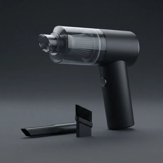 A compact handheld vacuum cleaner in matte black with a transparent dust bin, shown alongside a narrow attachment nozzle and a small cleaning brush on a dark gray studio background.