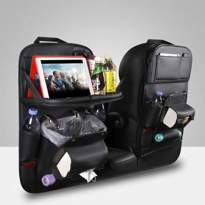 A black car seat backrest organizer shown installed on a vehicle seat, with storage pockets holding a tablet, bottles, tissues, and other small items. The product is photographed in a clean studio-style setting with no person or real environment visible.