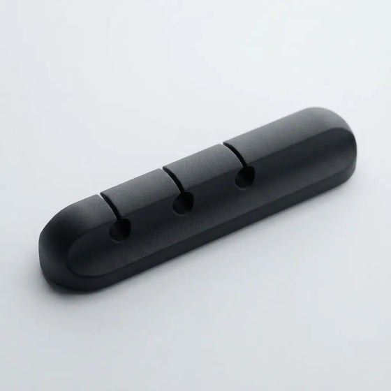A black plastic 3-hole cable guard or cable protector with a rounded rectangular shape, shown on a light gray background.