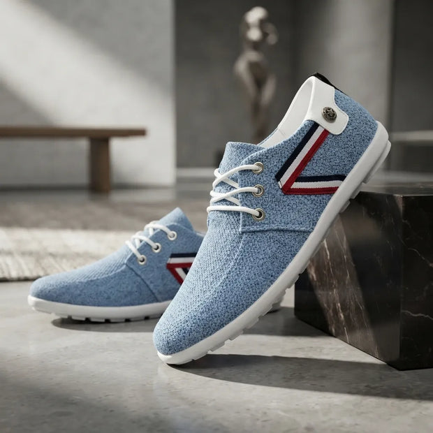 A pair of light blue knit lace-up sneakers with white soles and a red, white, and blue side stripe detail, displayed on a modern gray concrete floor next to a black marble block.