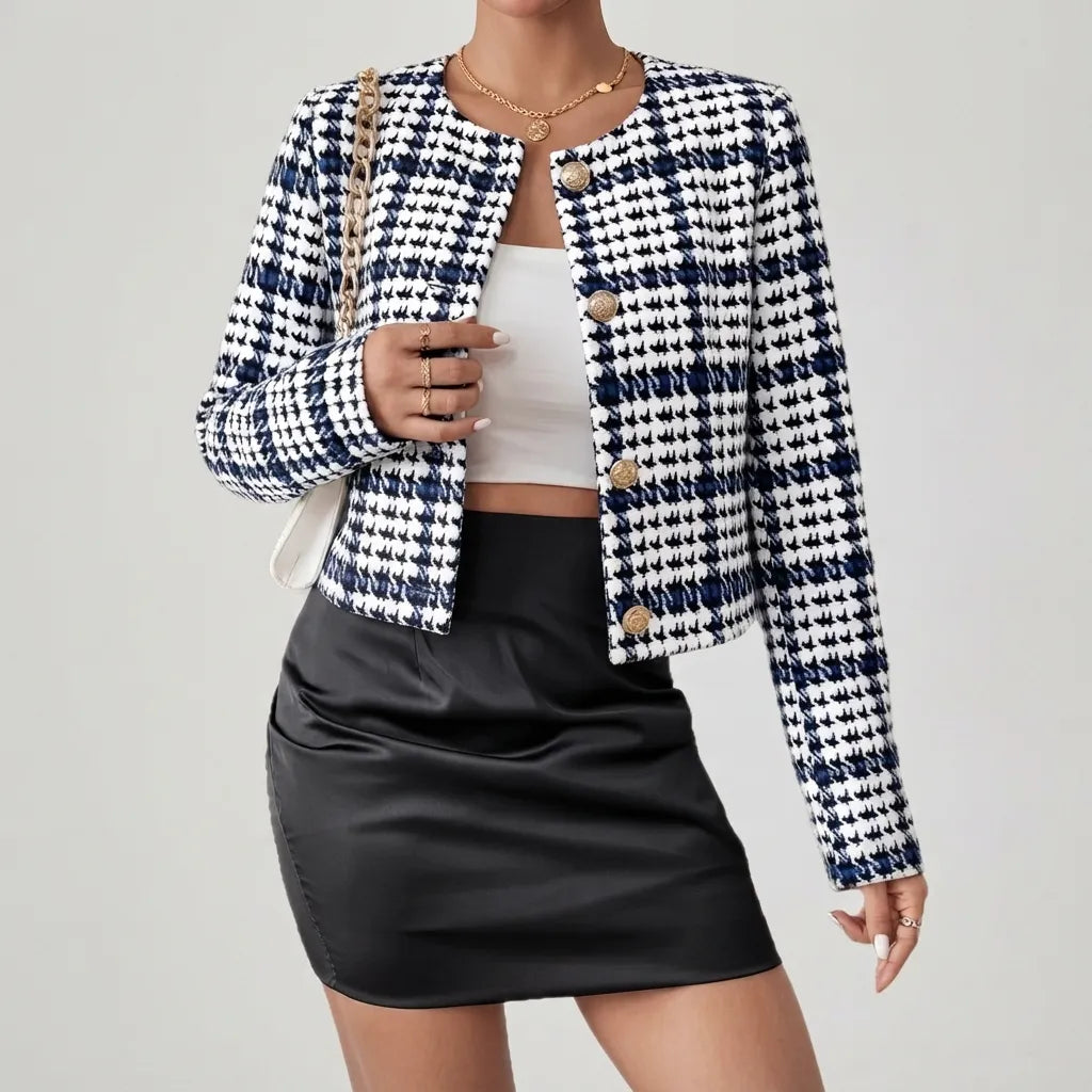 A woman models a cropped tweed jacket with a navy and white houndstooth pattern, styled with a black faux-leather mini skirt, a white crop top, and a gold chain bag against a light gray studio background.