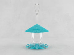 A bird feeder with a bright turquoise blue conical lid, a clear plastic cup in the center, and a matching turquoise base, suspended by a thin metal wire loop against a light gray background.