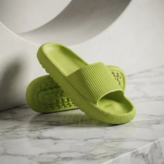 A pair of lime green textured slide sandals resting on a white marble surface with a modern white curved background.