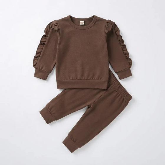 A toddler girl's two-piece clothing set in a solid medium brown color, featuring a long-sleeve sweatshirt with ruffled detailing on the sleeves and matching jogger pants, laid flat on a light gray background.