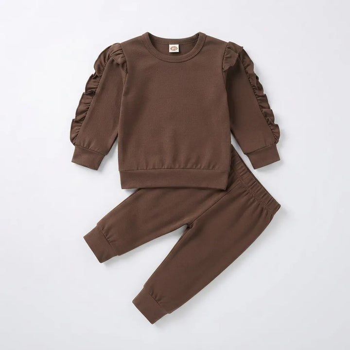 A toddler girl's two-piece clothing set in a solid medium brown color, featuring a long-sleeve sweatshirt with ruffled detailing on the sleeves and matching jogger pants, laid flat on a light gray background.