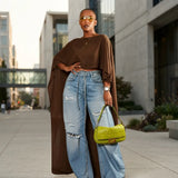 A woman stands on a city sidewalk wearing a brown draped long-sleeve top and light-wash wide-leg distressed jeans, holding a bright yellow-green crocodile-embossed handbag.