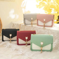 Five colorful handbags with cat-shaped charms on a soft surface.