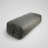 A dark gray rectangular yoga prop pillow with a textured fabric surface and a strap detail on one end, shown on a light gray background.
