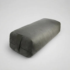 A dark gray rectangular yoga prop pillow with a textured fabric surface and a strap detail on one end, shown on a light gray background.