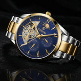 A luxury two-tone mechanical watch with a blue dial, gold-tone case details, and a silver-and-gold metal link bracelet, displayed on a dark reflective surface.