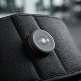A close-up of a circular black control module with red trim and directional buttons, mounted on a textured black padded surface.