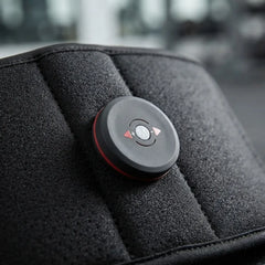 A close-up of a circular black control module with red trim and directional buttons, mounted on a textured black padded surface.