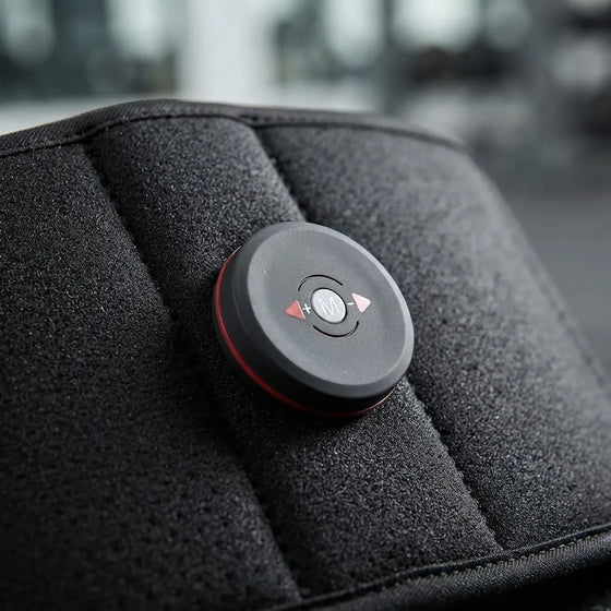 A close-up of a circular black control module with red trim and directional buttons, mounted on a textured black padded surface.