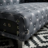 Close-up of a tufted upholstered bench or ottoman in dark gray fabric with a diamond button pattern, shown on a black-and-white geometric patterned rug.