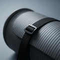 Close-up of a ribbed gray cylindrical product with a black strap and silver buckle, photographed on a soft gray background.
