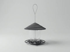 A modern bird feeder with a dark gray ribbed conical roof, a clear cylindrical body, and a circular base with a hanging loop, shown on a light gray background.