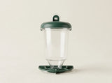A clear plastic cup with a dark green lid and matching green base, photographed against a plain light beige background.