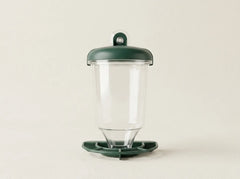 A clear plastic cup with a dark green lid and matching green base, photographed against a plain light beige background.