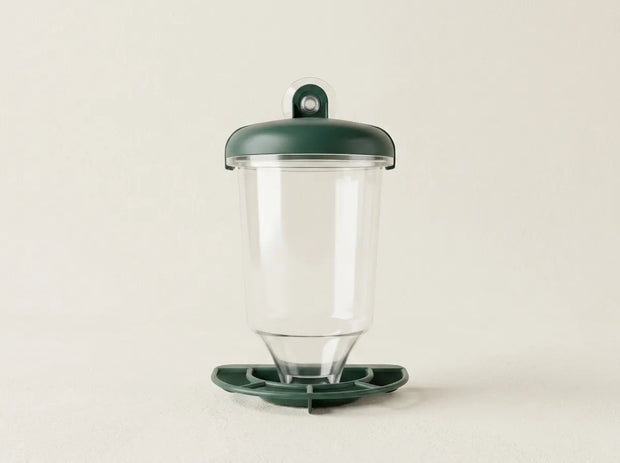 A clear plastic cup with a dark green lid and matching green base, photographed against a plain light beige background.