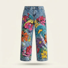 Light blue denim jeans with a vibrant, multicolored floral print, shown against a plain light beige background.