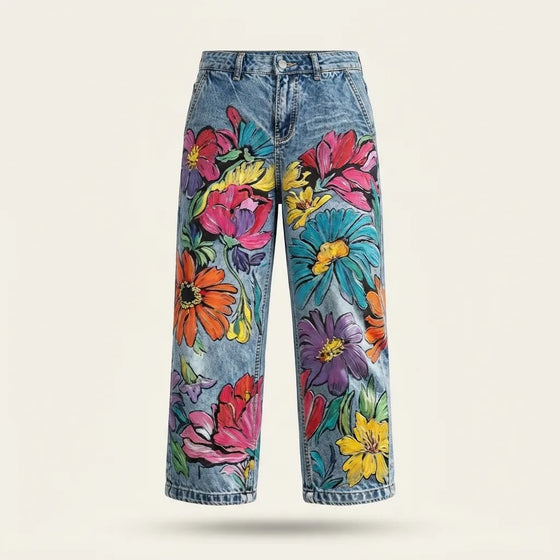Light blue denim jeans with a vibrant, multicolored floral print, shown against a plain light beige background.