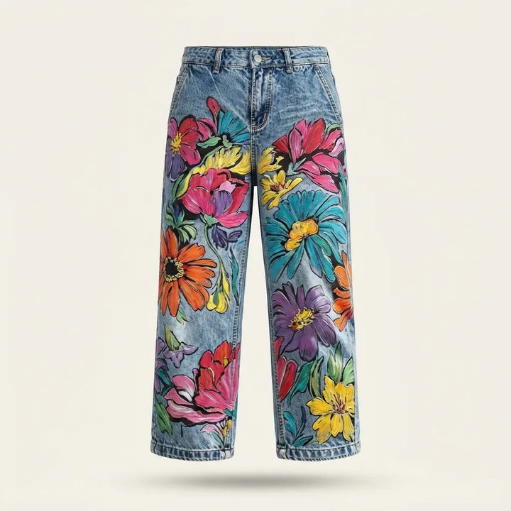 Light blue denim jeans with a vibrant, multicolored floral print, shown against a plain light beige background.