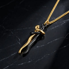 A gold chain necklace with a pendant featuring a black and gold abstract, wavy design, displayed on a dark marble surface.