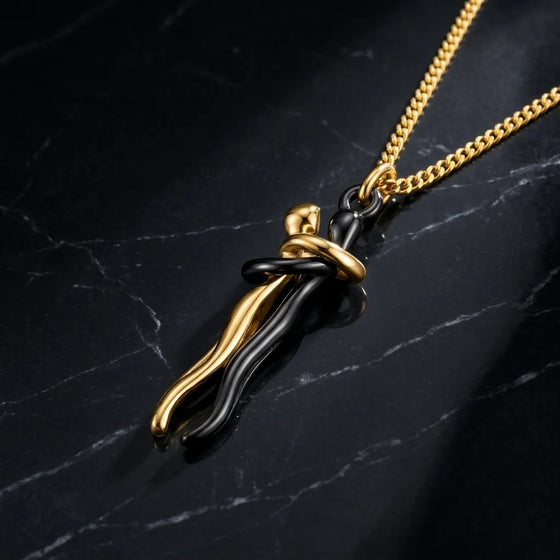 A gold chain necklace with a pendant featuring a black and gold abstract, wavy design, displayed on a dark marble surface.
