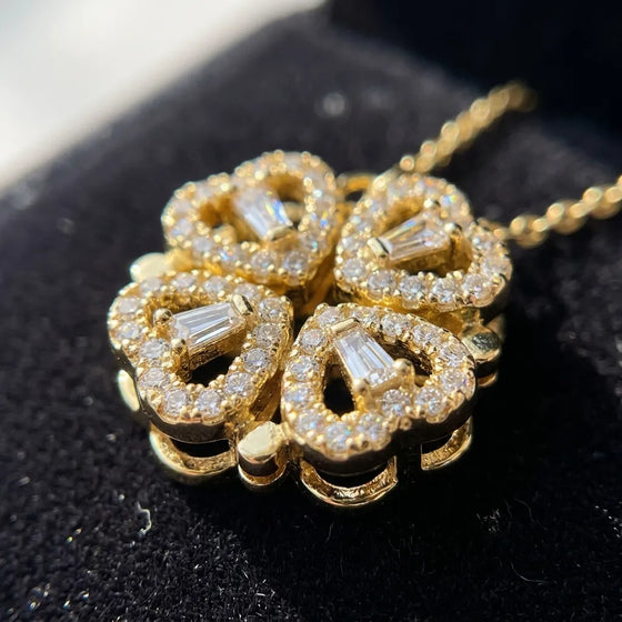 A gold four-leaf clover pendant necklace adorned with clear baguette and round-cut stones, resting on a black velvet jewelry box.