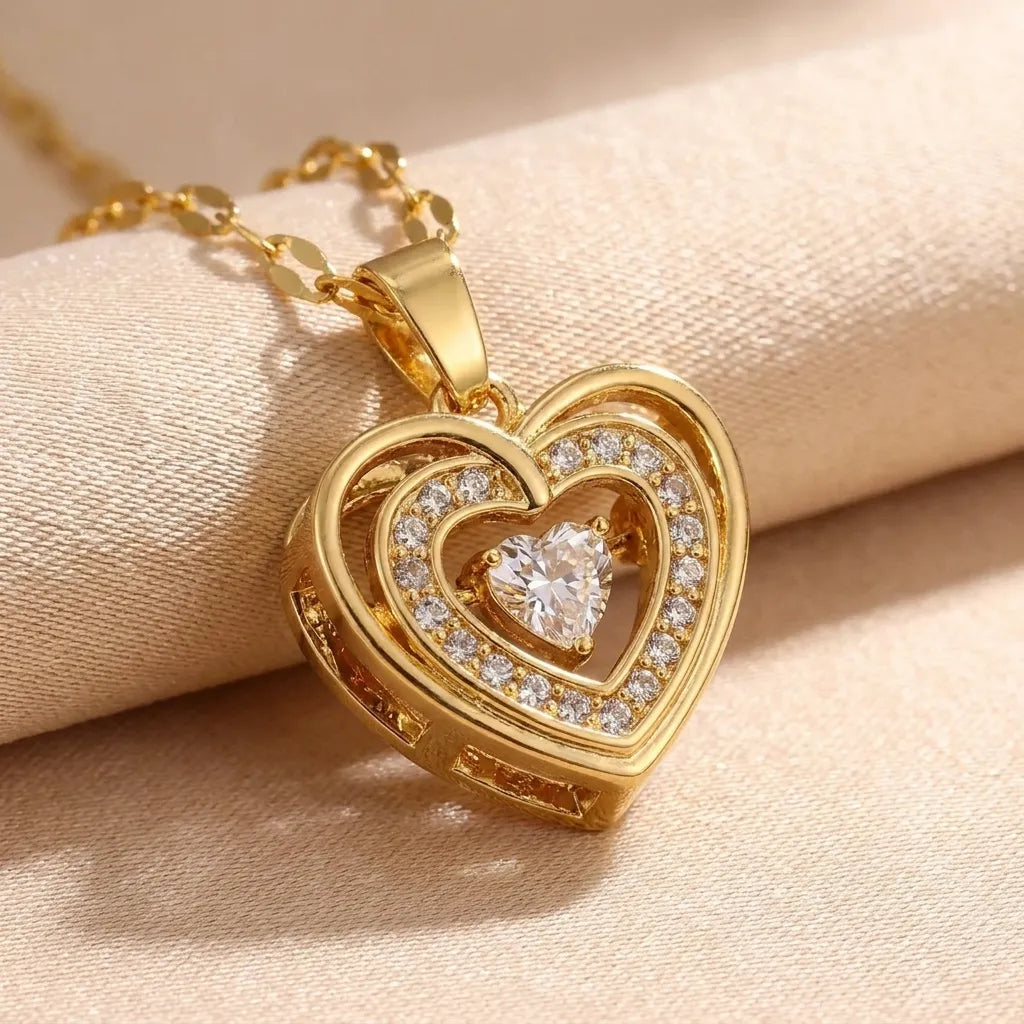 A gold heart-shaped pendant necklace with a double-heart design, set with clear crystals, resting on a beige fabric surface.