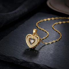 A gold heart-shaped pendant necklace with a clear central gemstone and small surrounding stones, displayed on a dark slate surface.