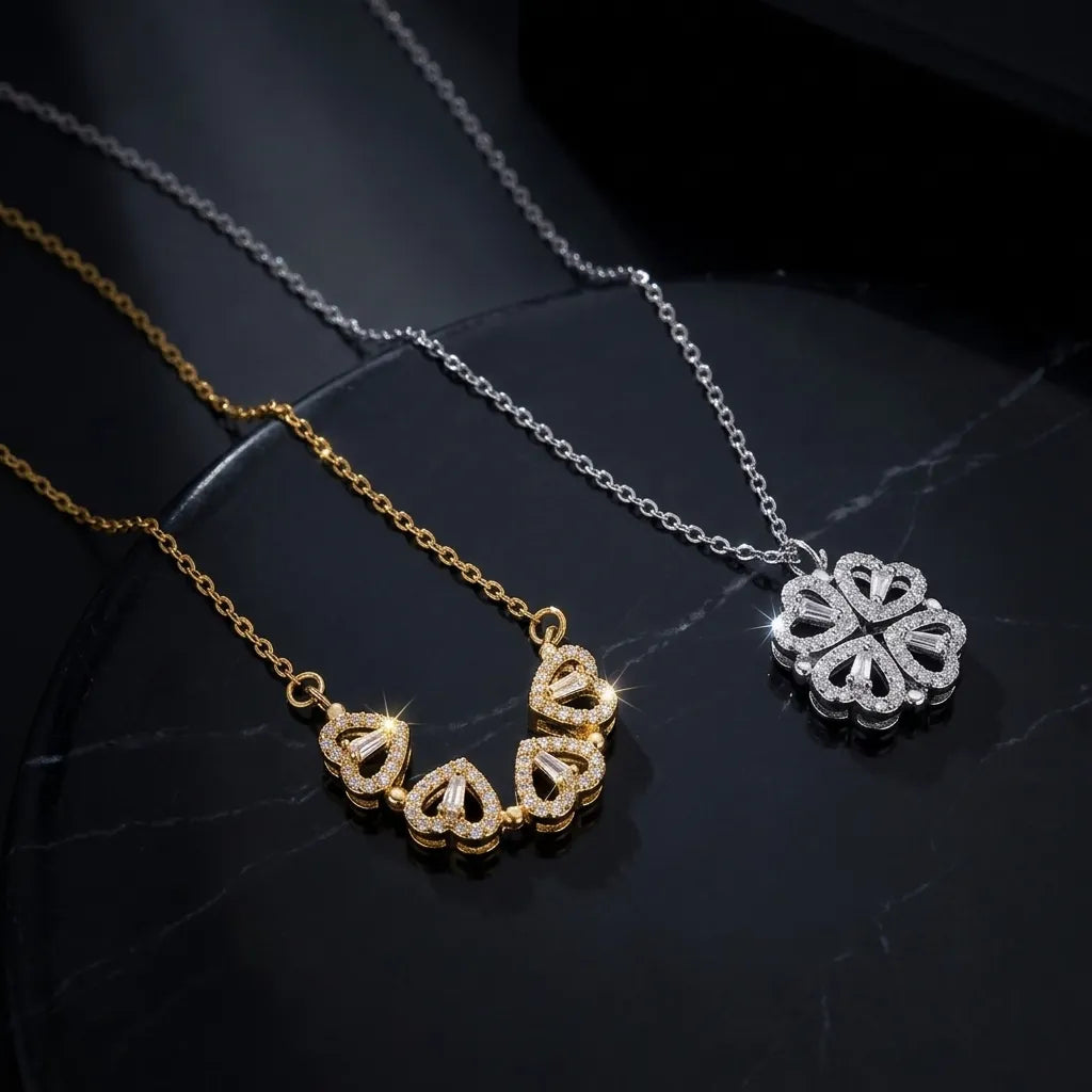Two delicate pendant necklaces displayed on a dark reflective surface: one gold-tone necklace with five small heart-shaped pavé pendants, and one silver-tone necklace with a large flower-shaped pavé pendant.