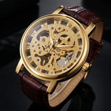 A luxury skeleton watch with a gold-tone case, intricate mechanical movement visible through the dial, and a dark brown leather strap, shown on a dark reflective surface.