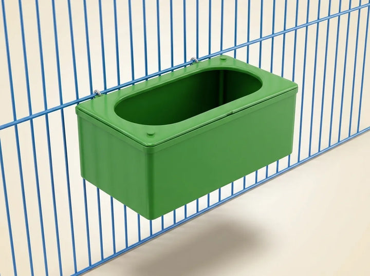 A green rectangular plastic hanging container with a rounded top, mounted against a blue wire cage on a light background.