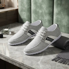 A pair of light gray textured lace-up shoes with white soles and white laces, displayed on a gray marble tabletop with a green paneled background and a folded gray scarf.
