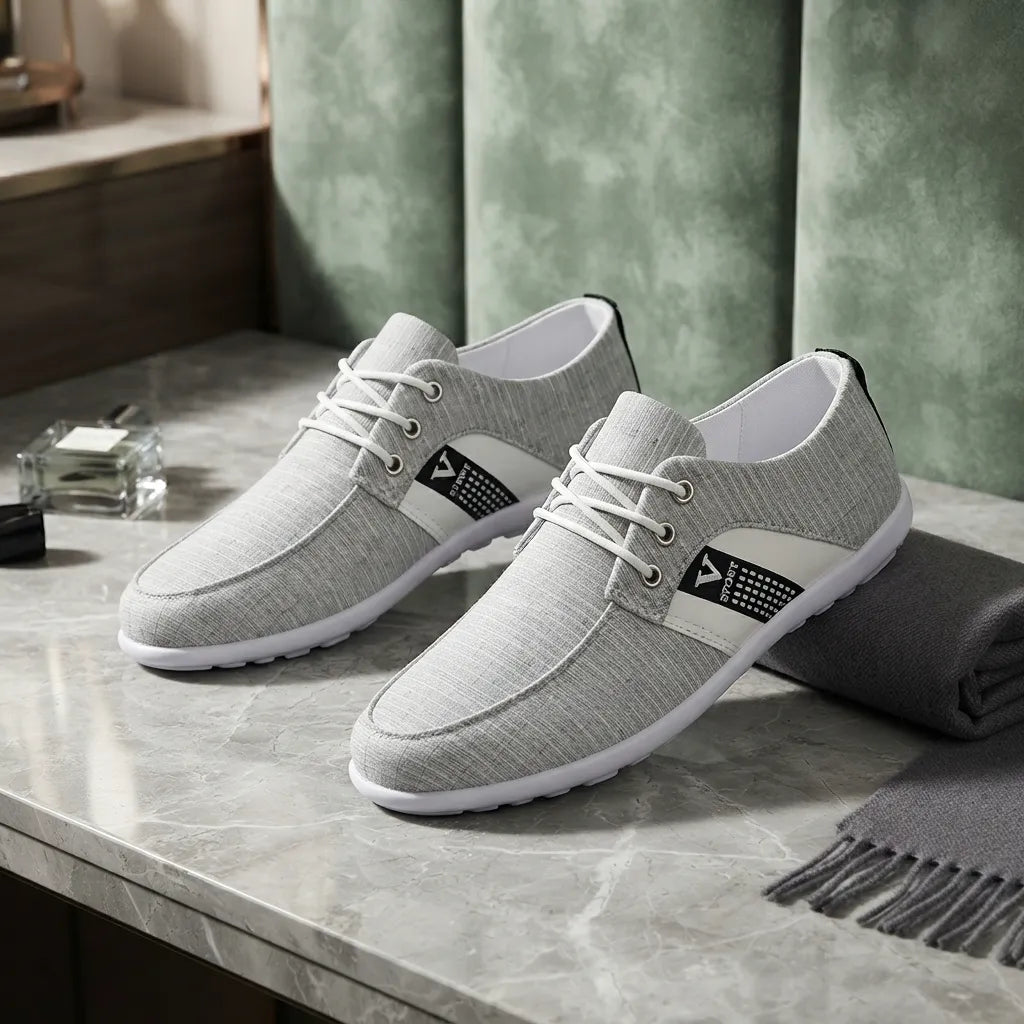 A pair of light gray textured lace-up shoes with white soles and white laces, displayed on a gray marble tabletop with a green paneled background and a folded gray scarf.