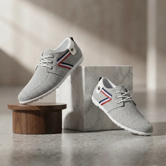 A pair of light gray knit lace-up sneakers displayed on a marble block and wooden pedestal against a softly lit neutral background.