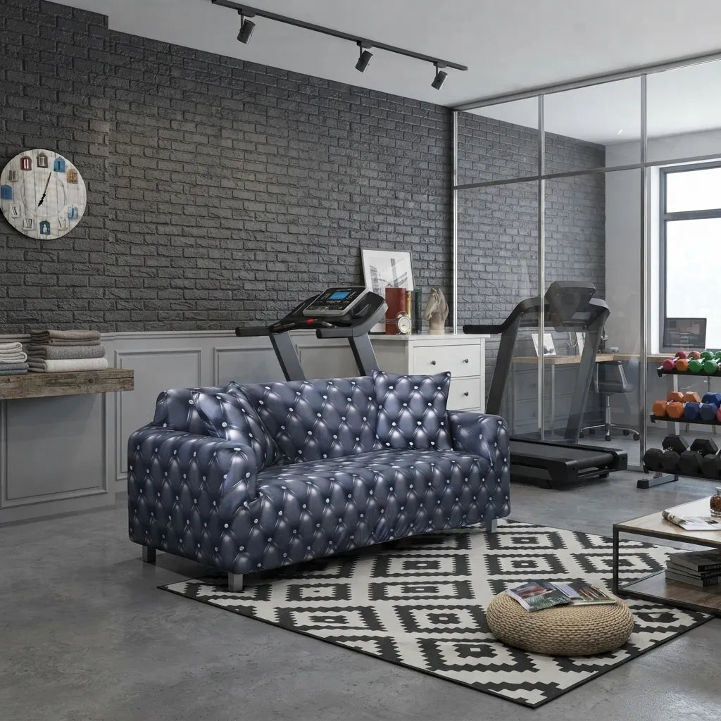 A tufted loveseat sofa in a dark blue-gray leather or faux leather, styled in a modern home gym setting with treadmills, a brick wall, and a geometric rug.
