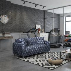 A tufted loveseat sofa in a dark blue-gray leather or faux leather, styled in a modern home gym setting with treadmills, a brick wall, and a geometric rug.