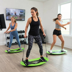 Three women exercise indoors on bright green and black board-walking devices in a fitness studio with wood floors, dumbbells, and a window.