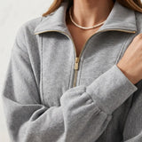Close-up of a person wearing a heather gray quarter-zip pullover with a stand collar and gold-tone zipper hardware.