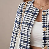 A close-up of a person wearing a black and white houndstooth tweed jacket with gold buttons, a white top, and a white handbag with a gold chain strap.
