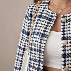 A close-up of a person wearing a black and white houndstooth tweed jacket with gold buttons, a white top, and a white handbag with a gold chain strap.