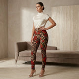 A woman stands in a styled indoor room wearing high-waisted leopard-print and red floral leggings with a cream mock-neck top and clear high-heel sandals.